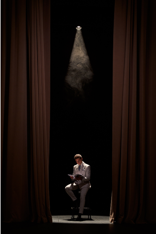 Person seated under a spotlight on a dark stage